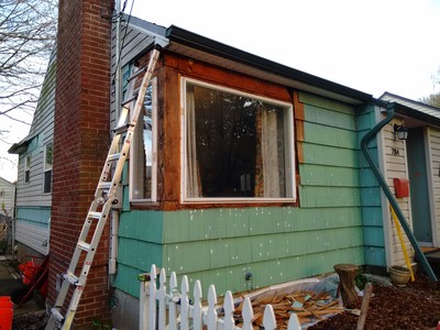 After removing shingles from the corner between the two windows, patching nail holes, and one coat of primer. The vinyl removed back past the chimney was for cellulose insulation we had blown into the wall cavities from the outside.
